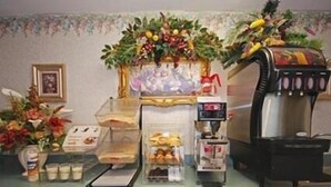 Et tekøkken med kaffemaskine, køleskab og mikrobølgeovn. Der er også to blomsterarrangementer og et indrammet billede på bordpladen.