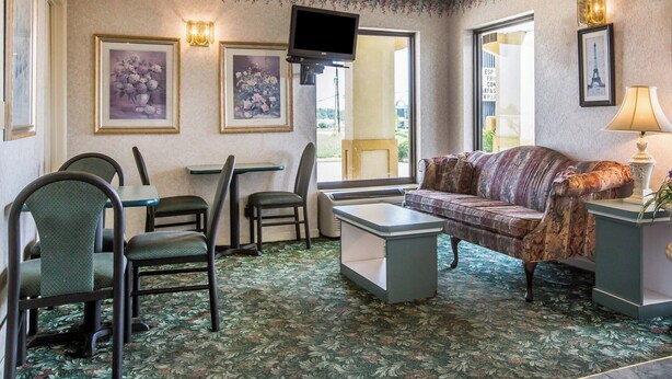 Et hotelværelse med sofa, stole, et lille bord, et fjernsyn og billedkunst på væggene.