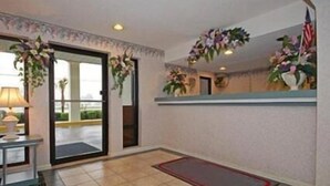 Et hotel lobby med fliset gulv, en receptionsdisk med lampe og dekorative planter.