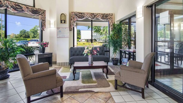 A spacious indoor area with a sofa, two armchairs, a coffee table, and a potted plant. - Econo Lodge Garner - Raleigh (Garner)