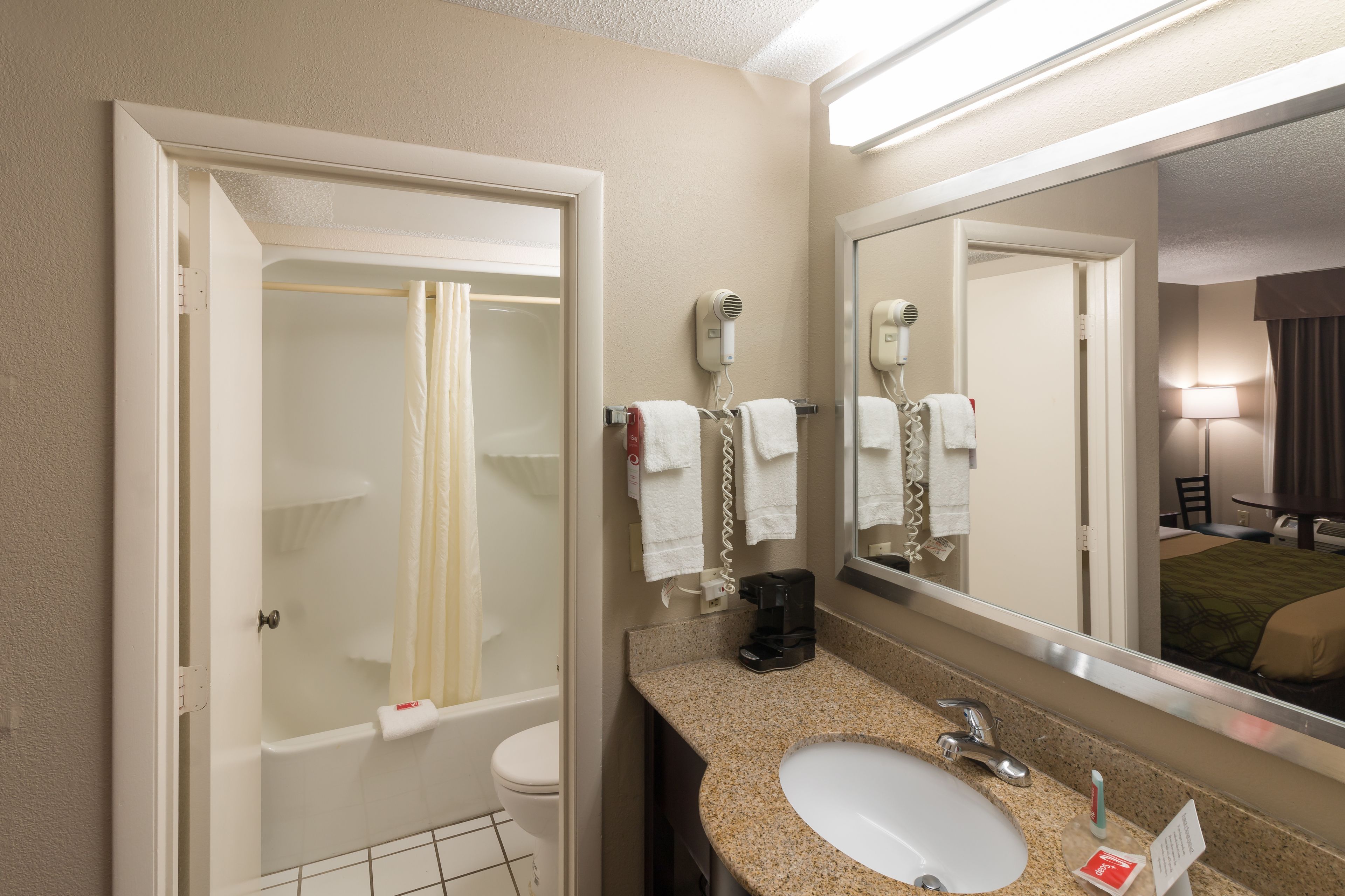 A hotel bathroom with a shower, toilet, sink, and a large mirror.