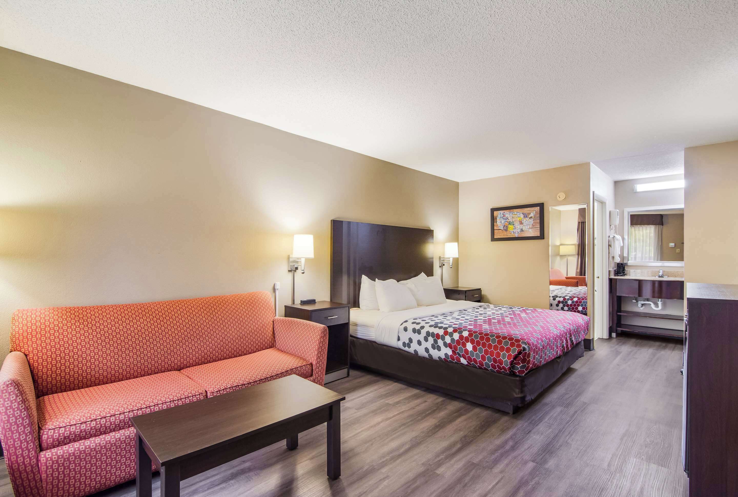 A hotel room with a sofa, a bed with a patterned bedspread, a nightstand, a desk, and a dresser.