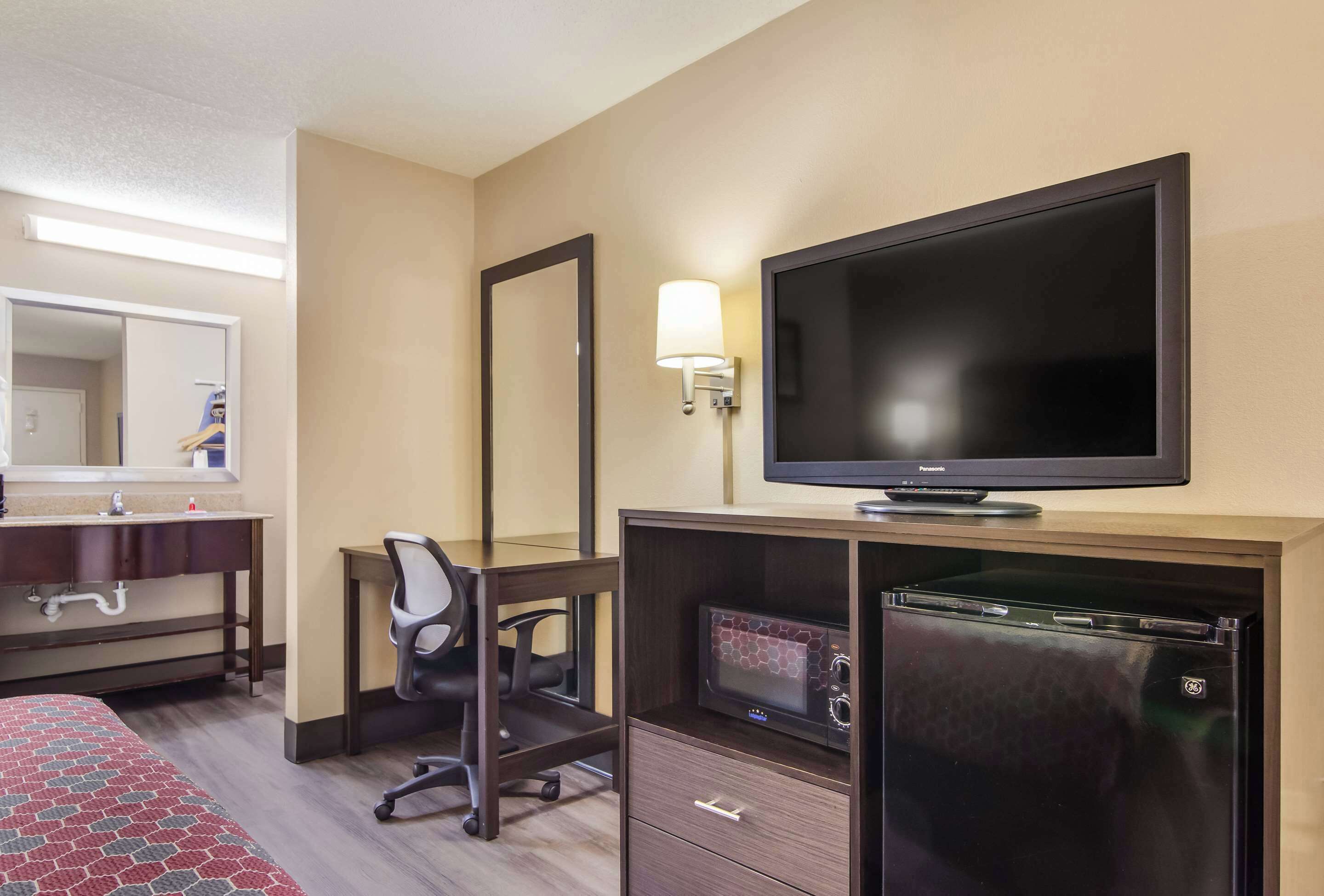Habitación de hotel con una cama, un escritorio con silla, televisión, microondas y refrigerador.