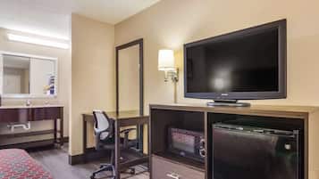 Habitación de hotel con una cama, un escritorio con silla, televisión, microondas y refrigerador.