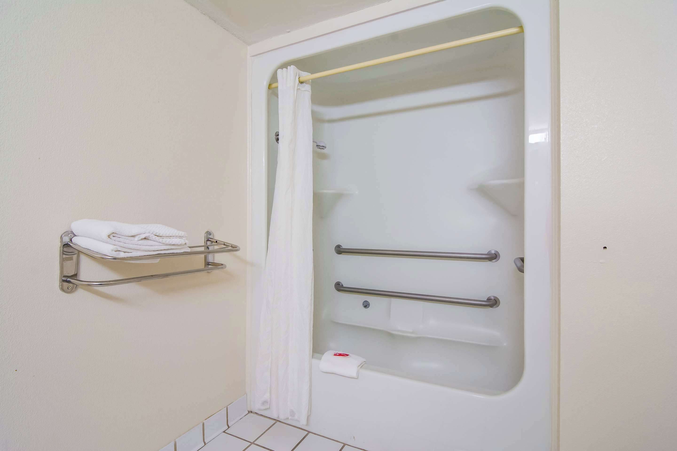 A bathroom with a white bathtub, a shower curtain, a towel rack with folded towels, and a grab bar for support.