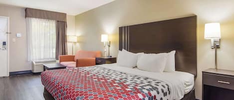 A hotel room with a large bed, a desk, a chair, and a window with curtains.