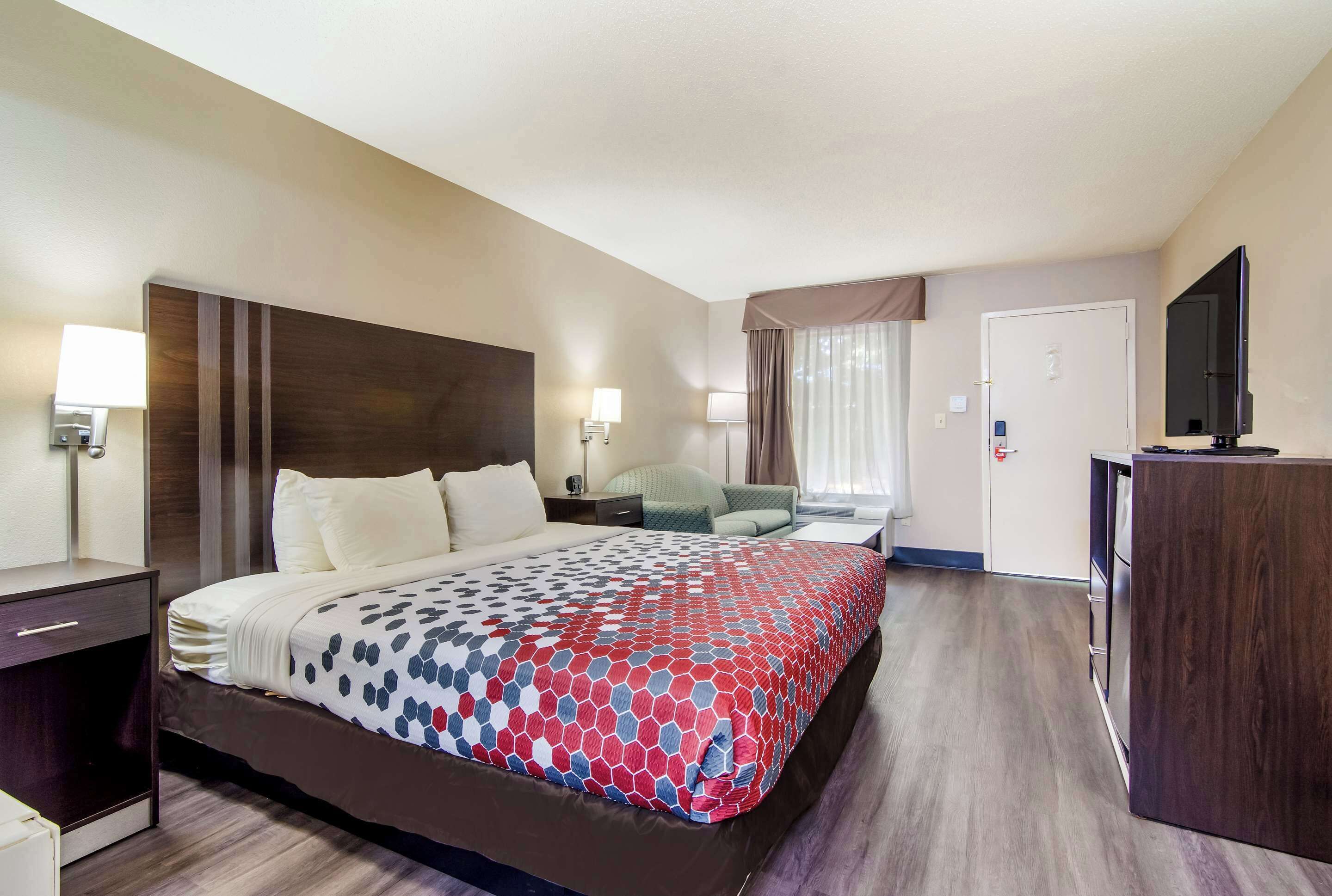 A hotel room with a large bed, bedside tables, a desk, a chair, a television, and a wardrobe.