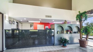 A reception area with a black marble counter, a red wall, and a large potted plant. - Econo Lodge Garner - Raleigh (Garner)