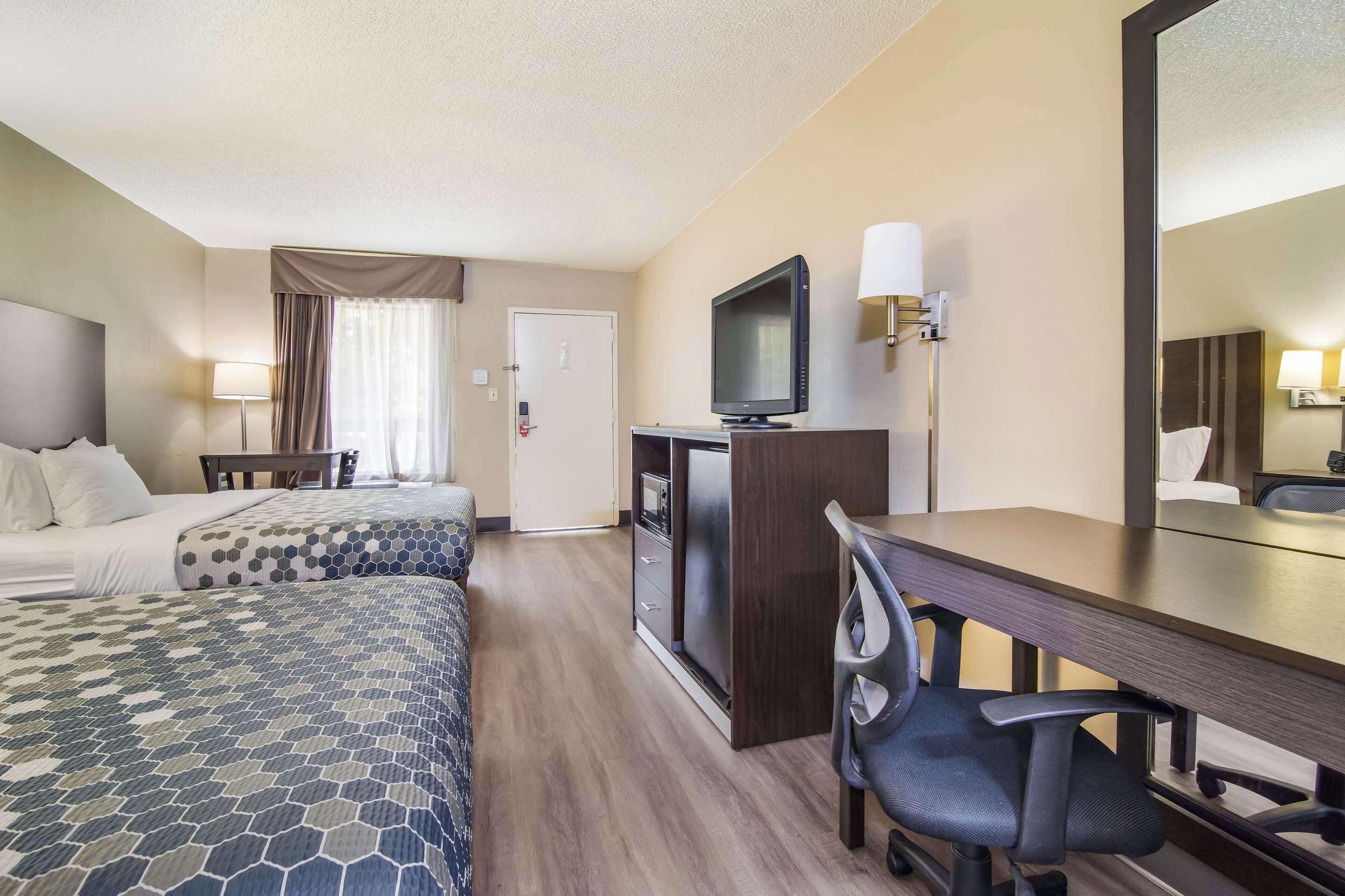 A hotel room with two beds, a desk, a TV, and a mirror.