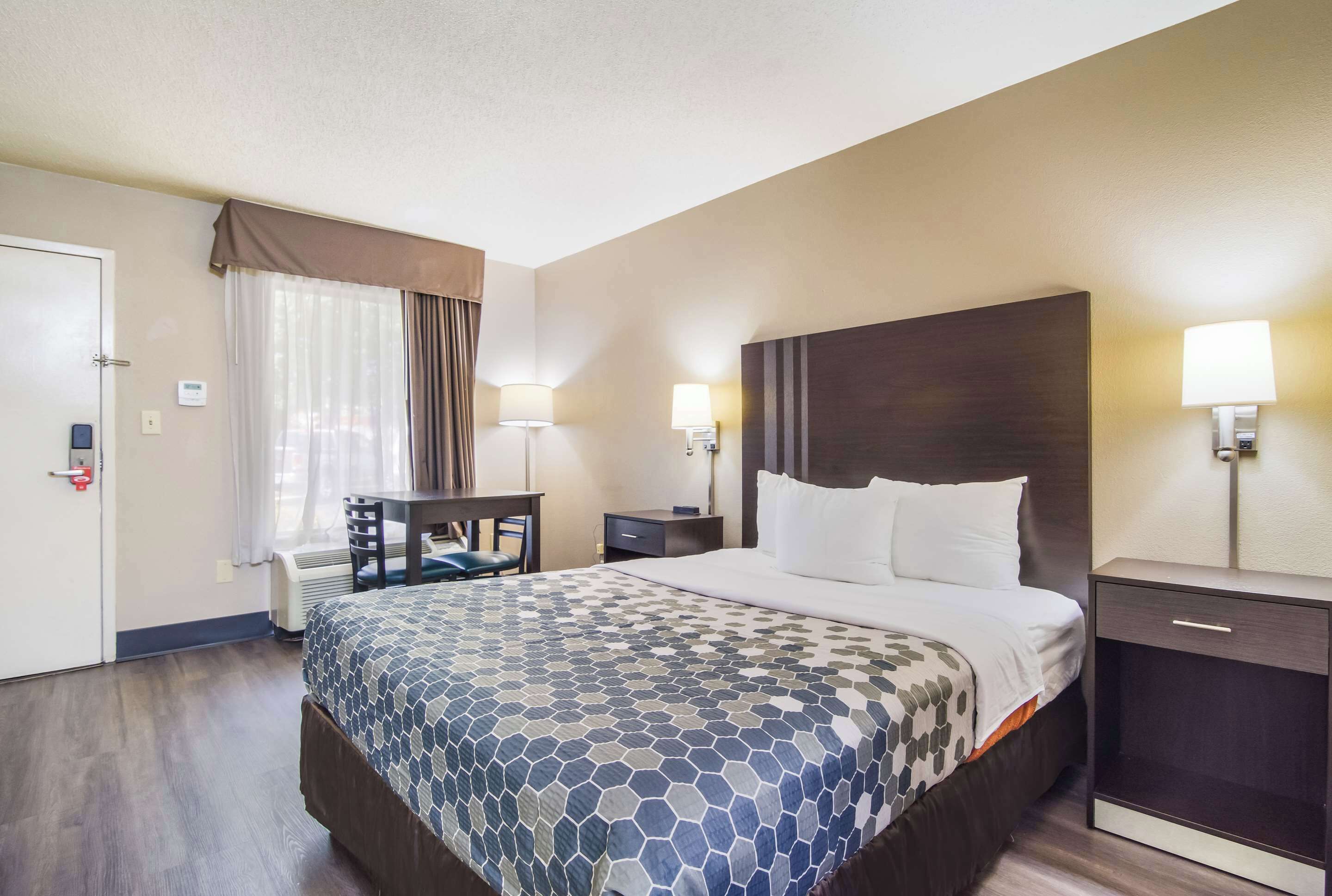 Habitación de hotel con una cama grande, un escritorio, dos lámparas de noche y una ventana con cortinas.