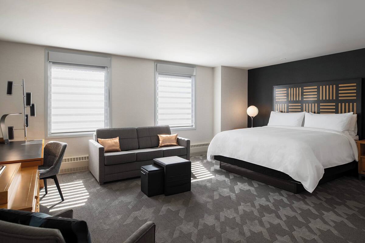 A modern hotel room with a large bed, a sofa, a desk, and a chair.