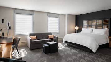 A modern hotel room with a large bed, a sofa, a desk, and a chair.