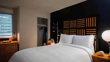 A hotel room with a large bed, a bedside table with a lamp, a wardrobe, and a window with blinds.