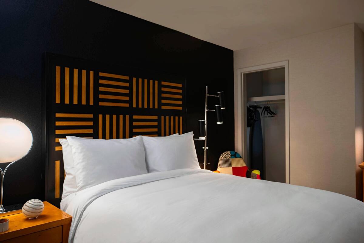 A modern hotel room with a large bed, a bedside lamp, a wardrobe, and a window with blinds.