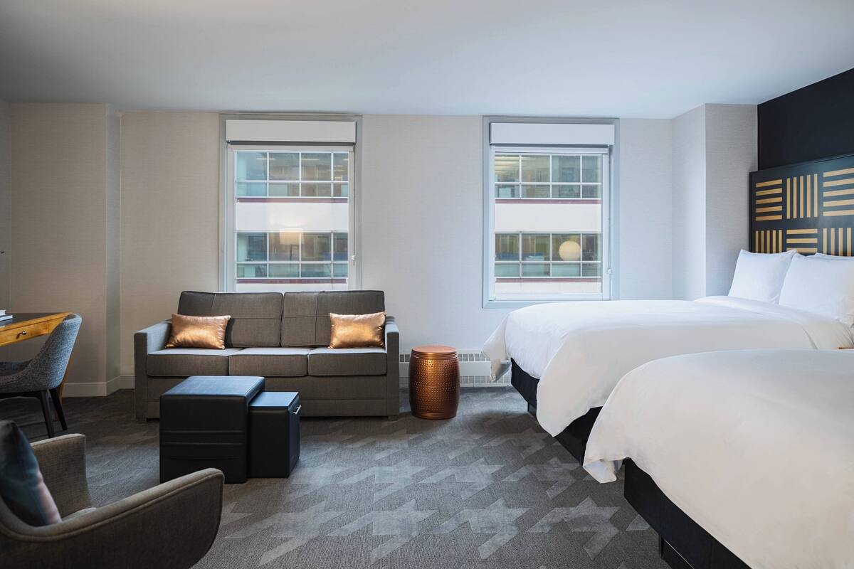 A hotel room with a sofa, two beds, a desk, and a chair.
