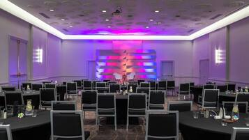 A conference room with round tables, black chairs, and a stage with a colorful backdrop.