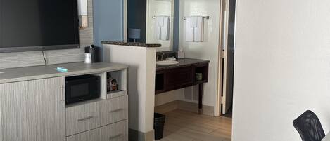 A compact living space with a kitchenette, a flat-screen TV, a microwave, and a patterned sofa.