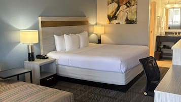 Quarto de hotel com uma cama, duas luminárias de cabeceira, uma escrivaninha, uma cadeira e um banquinho estampado.