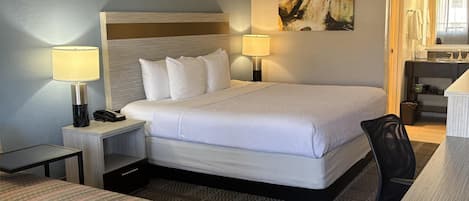 A hotel room with a bed, two bedside lamps, a desk, a chair, and a patterned ottoman.