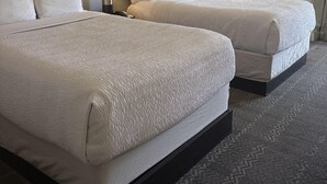Une chambre d’hôtel avec deux lits, une tête de lit, une lampe et une fenêtre avec des rideaux.