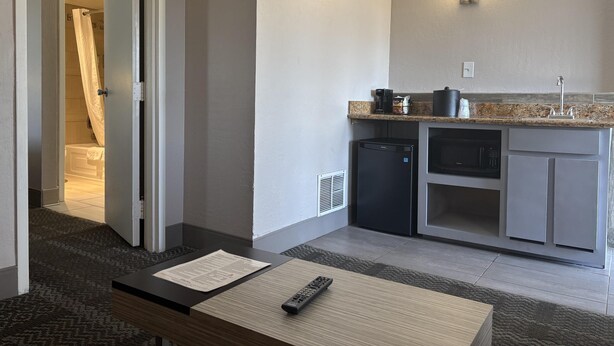 Une chambre d’hôtel avec une kitchenette, une salle de bain avec un rideau de douche et une télécommande posée sur une table.