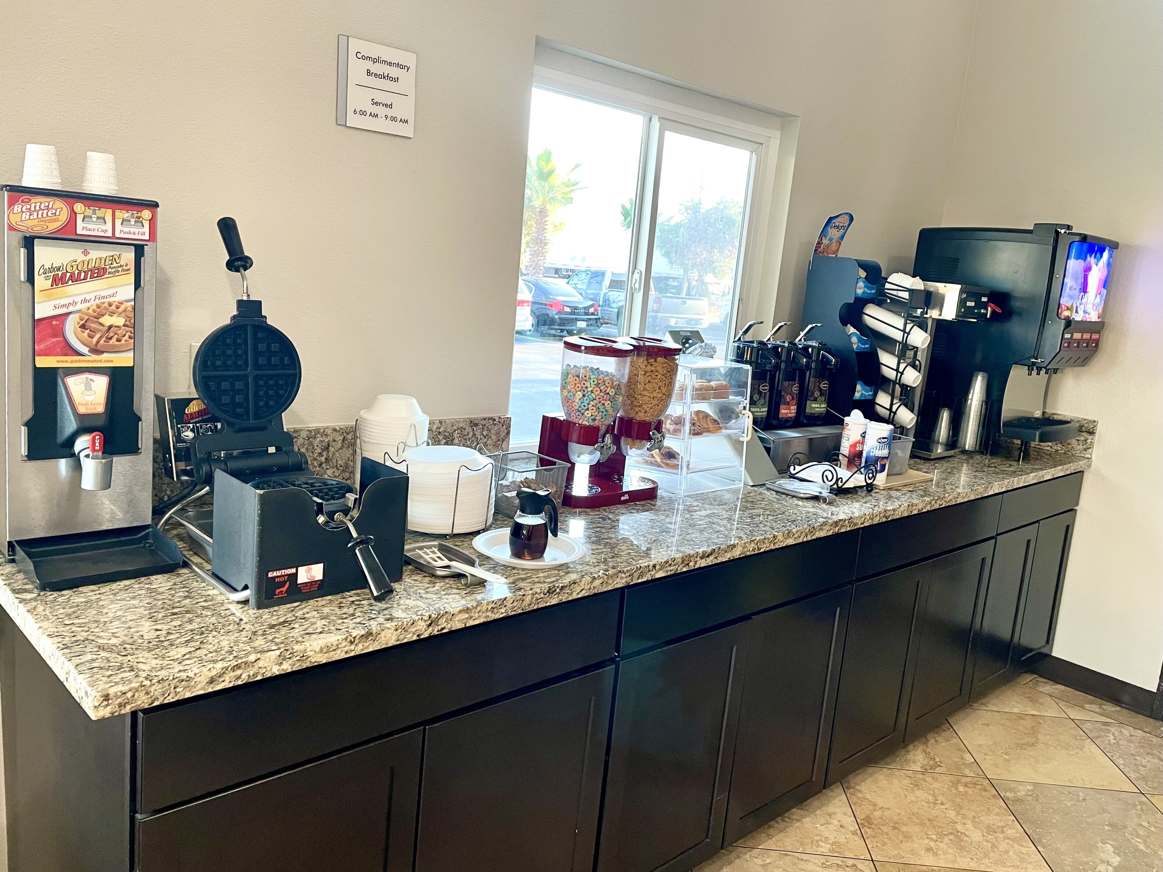 Una colazione a buffet con macchinette per waffle, macchine da caffè e un cartello che indica la colazione inclusa.