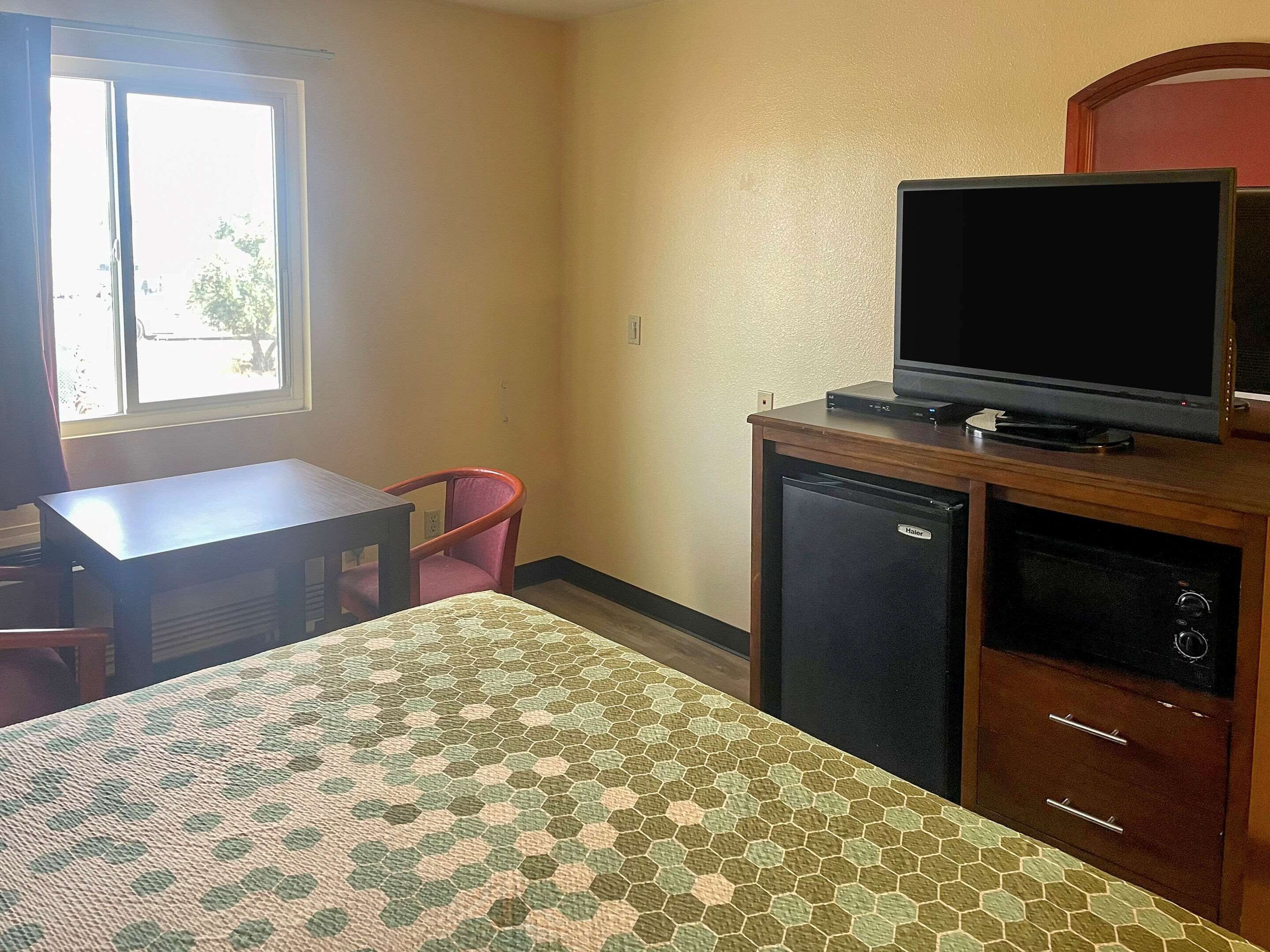 A hotel room with a bed, a desk, a chair, a television, and a refrigerator.