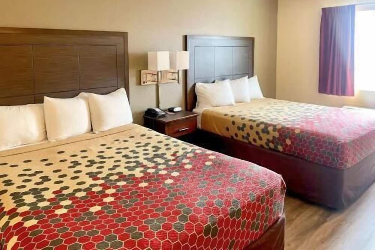 A hotel room with two beds, each with a headboard, bedside tables, lamps, and a window with curtains.