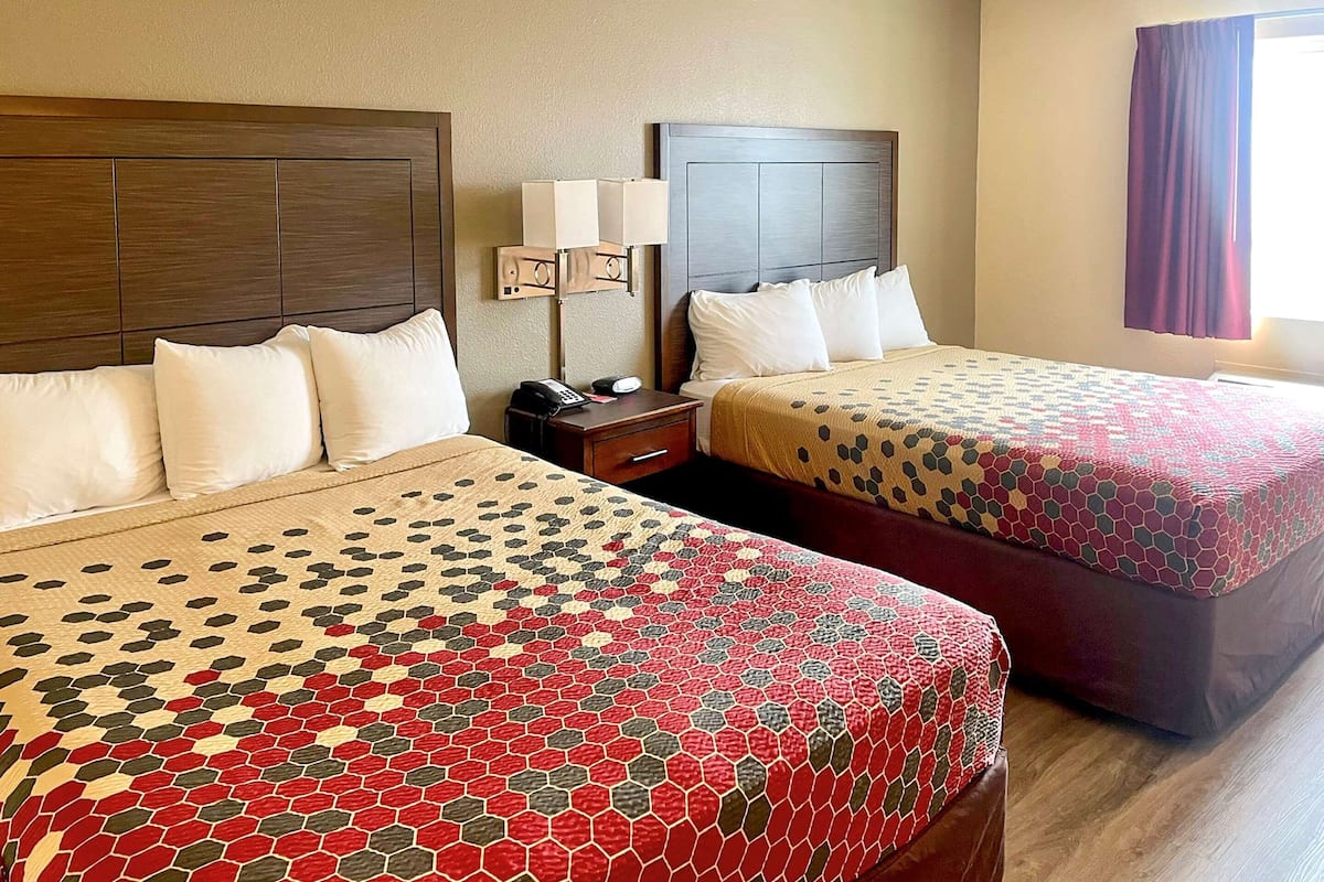 A hotel room with two beds, each with a patterned bedspread, a nightstand with a lamp, and a window with curtains.