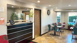 A hotel reception area with a check-in counter, a clock, and a dining area with tables and chairs. - Econo Lodge Inn & Suites Corning Travel Center (Corning)