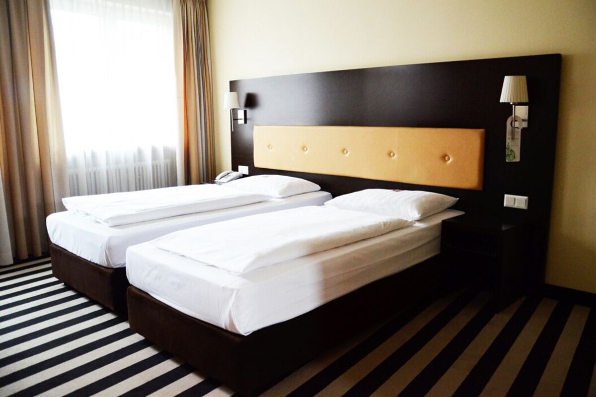 Une chambre d’hôtel avec deux lits, un sol à rayures et une tête de lit sombre.