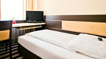Una habitación de hotel con una cama, un televisor en un soporte, una mesita pequeña y una silla.
