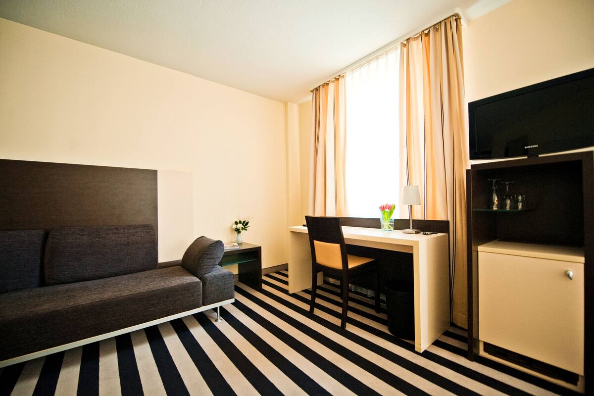 Una habitación de hotel moderna con sofá, escritorio y televisor.