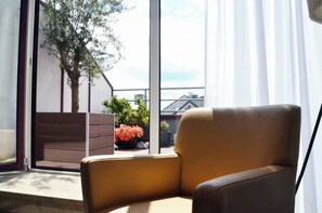 Ein Zimmer mit großem Fenster, einem braunen Sessel, einem Blumentopf und einer Treppe, die nach draußen führt.