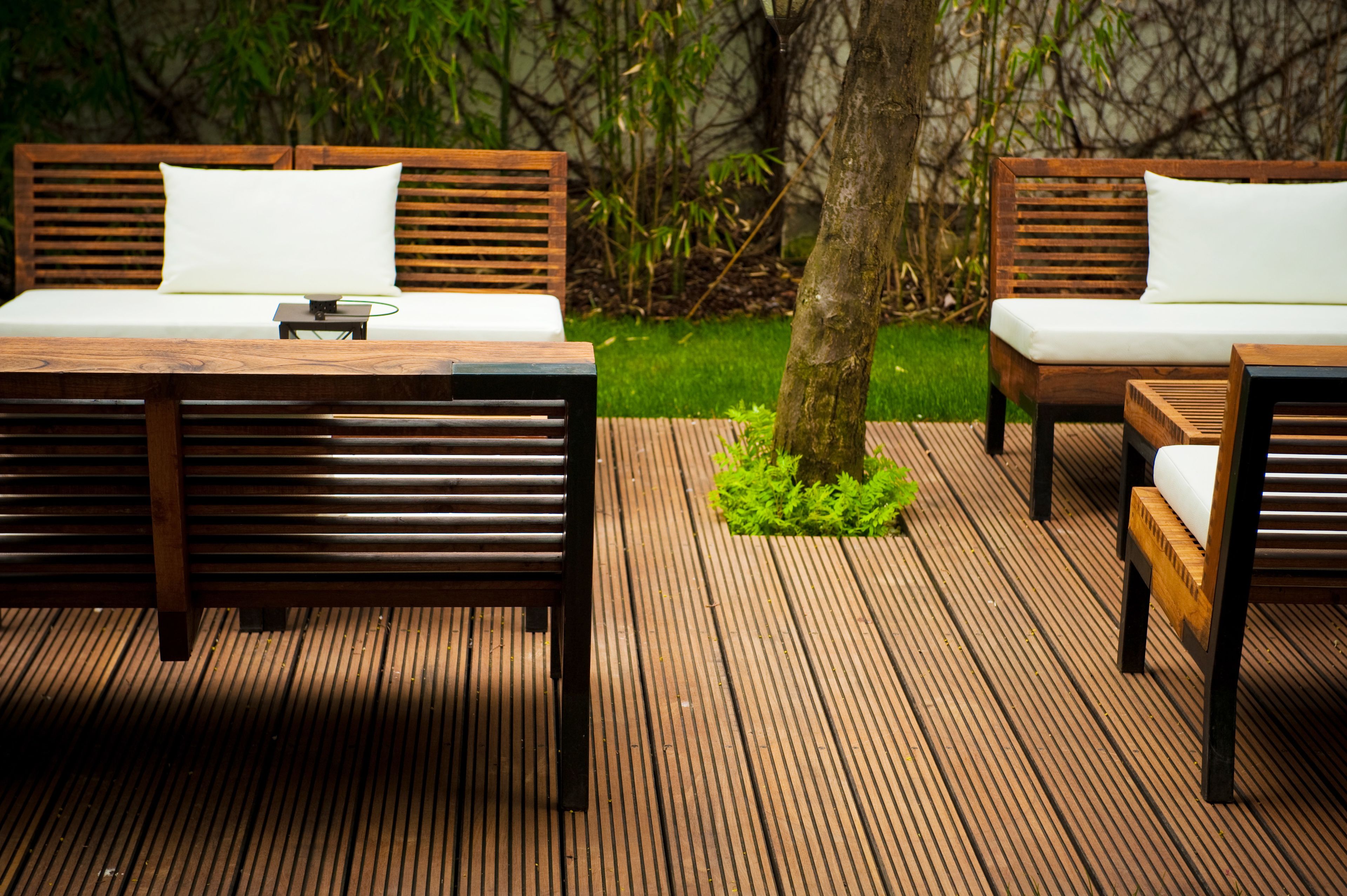 Eine Holzterrasse mit zwei Sofas und einem Tisch, umgeben von viel Grün.