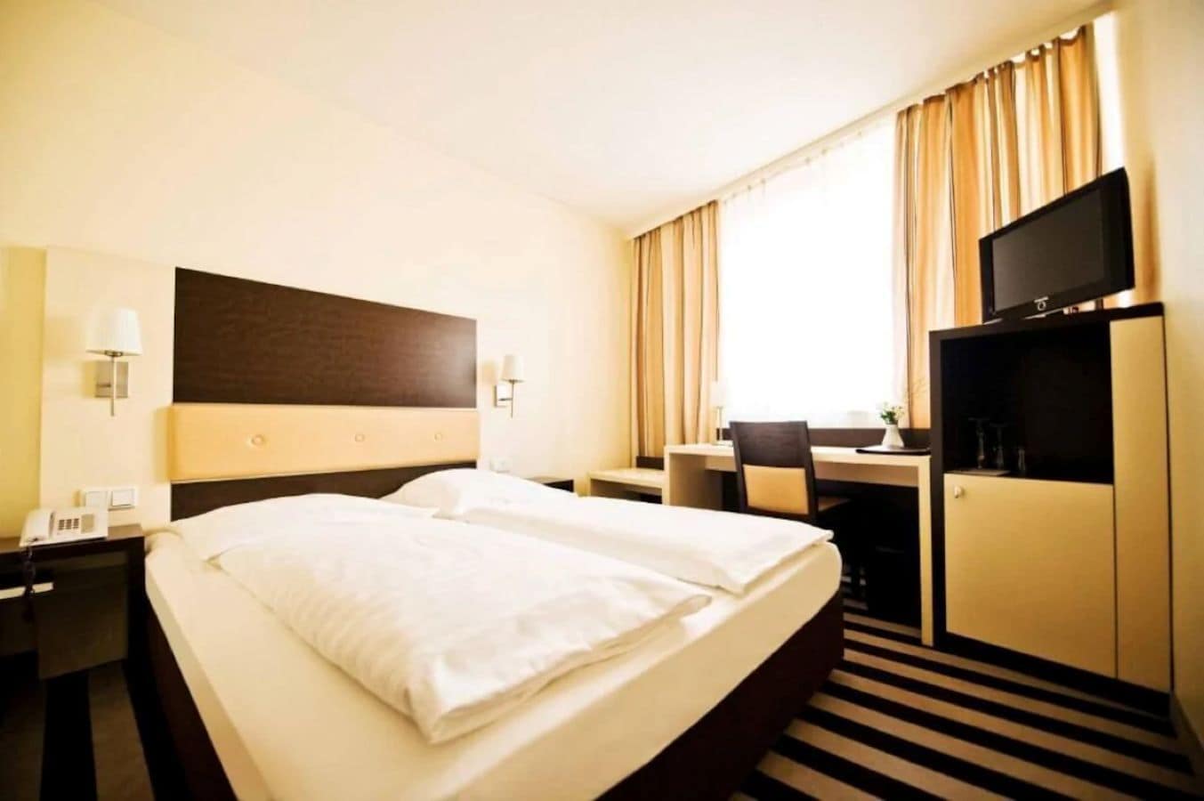 Una camera d'albergo con un letto grande, una scrivania, una sedia, un televisore e un minibar.