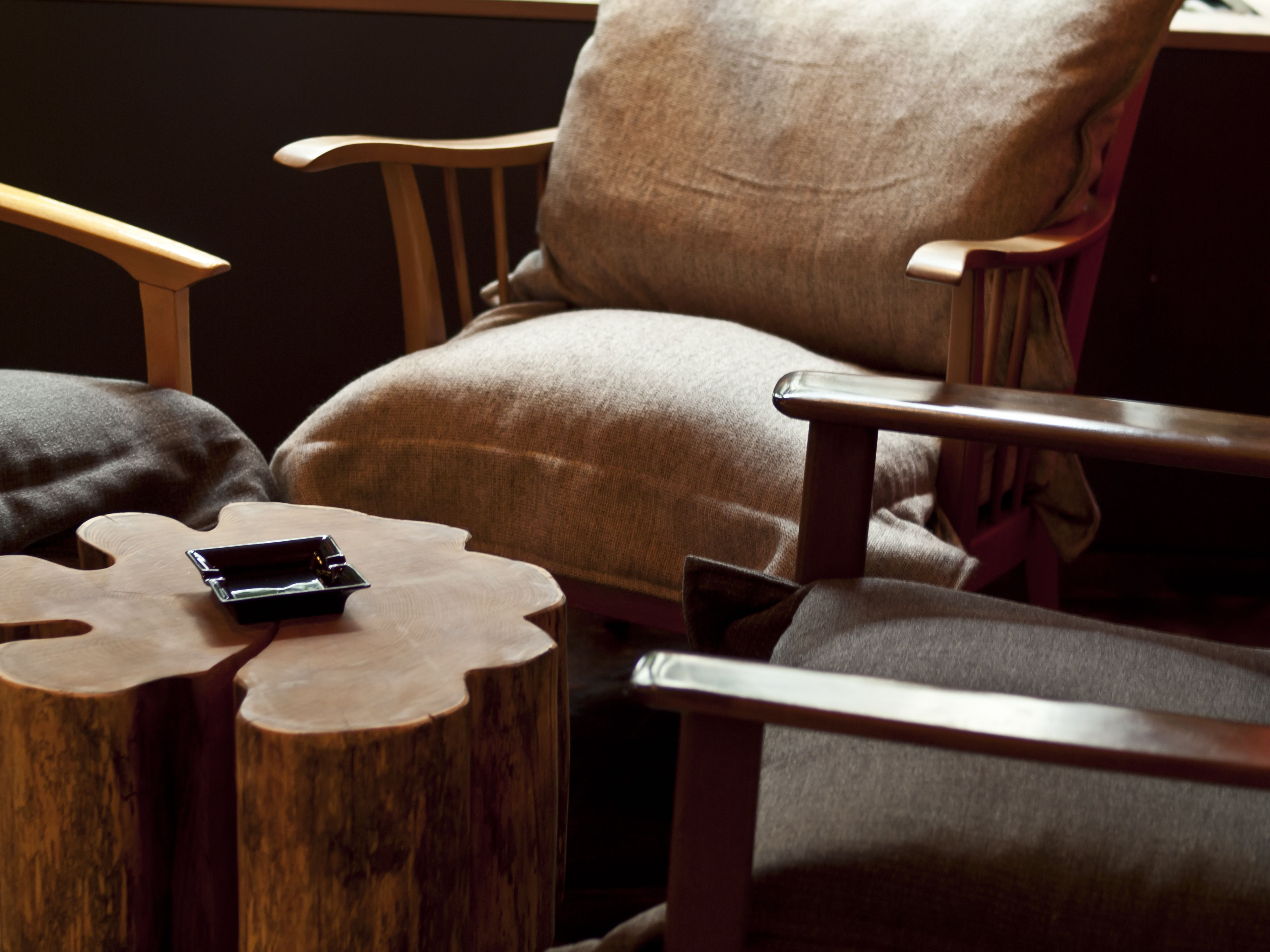 Un sillón de madera con cojín, una mesita de noche de madera con un teléfono inteligente encima y una silla de madera con cojín.