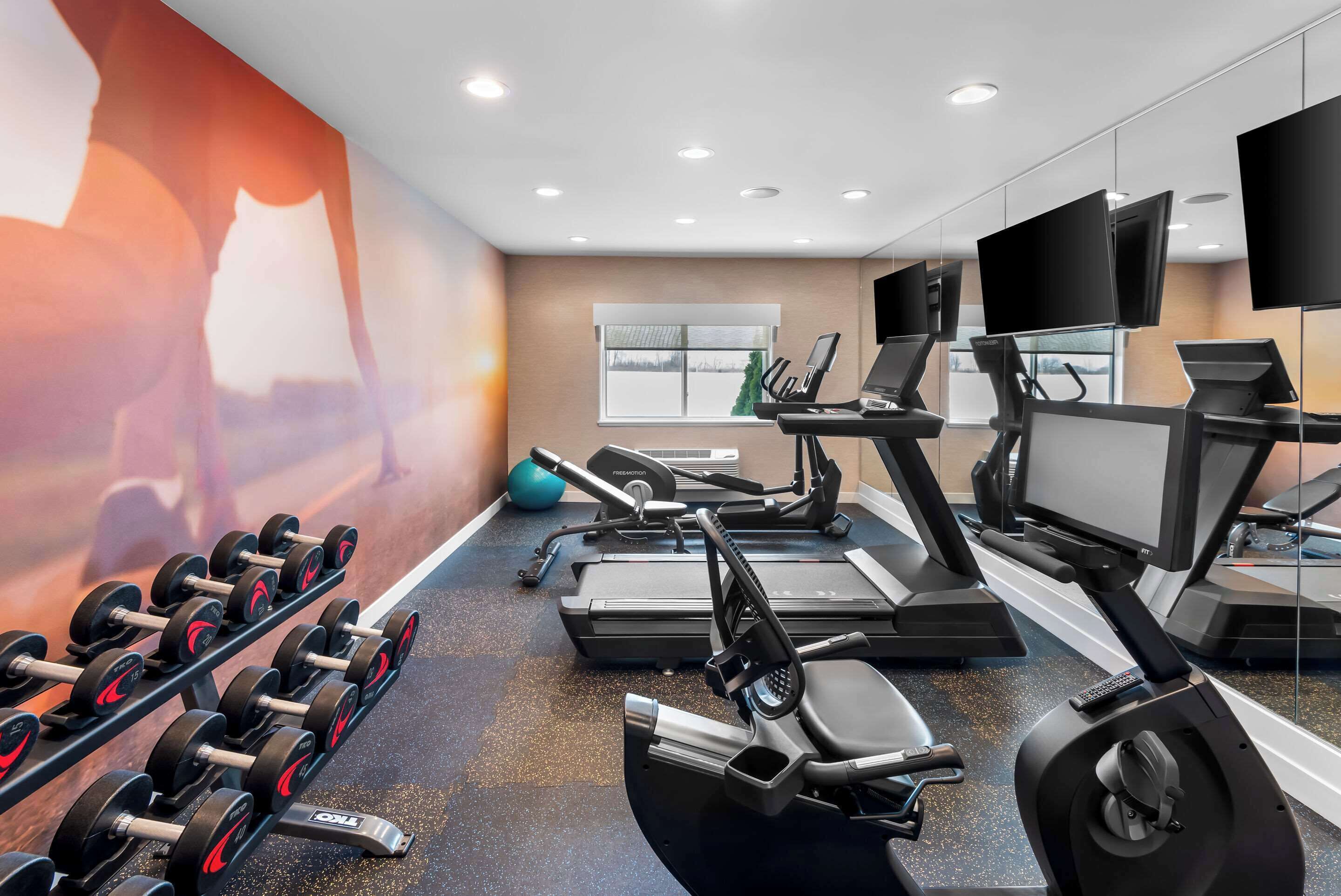 A gym with treadmills, elliptical machines, and dumbbells.