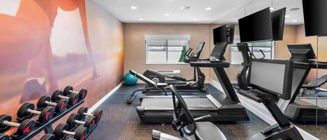 A gym with treadmills, elliptical machines, and dumbbells.