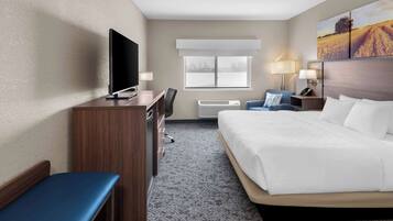 A hotel room with a bed, a desk with a TV, a chair, a lamp, and a window with a view.