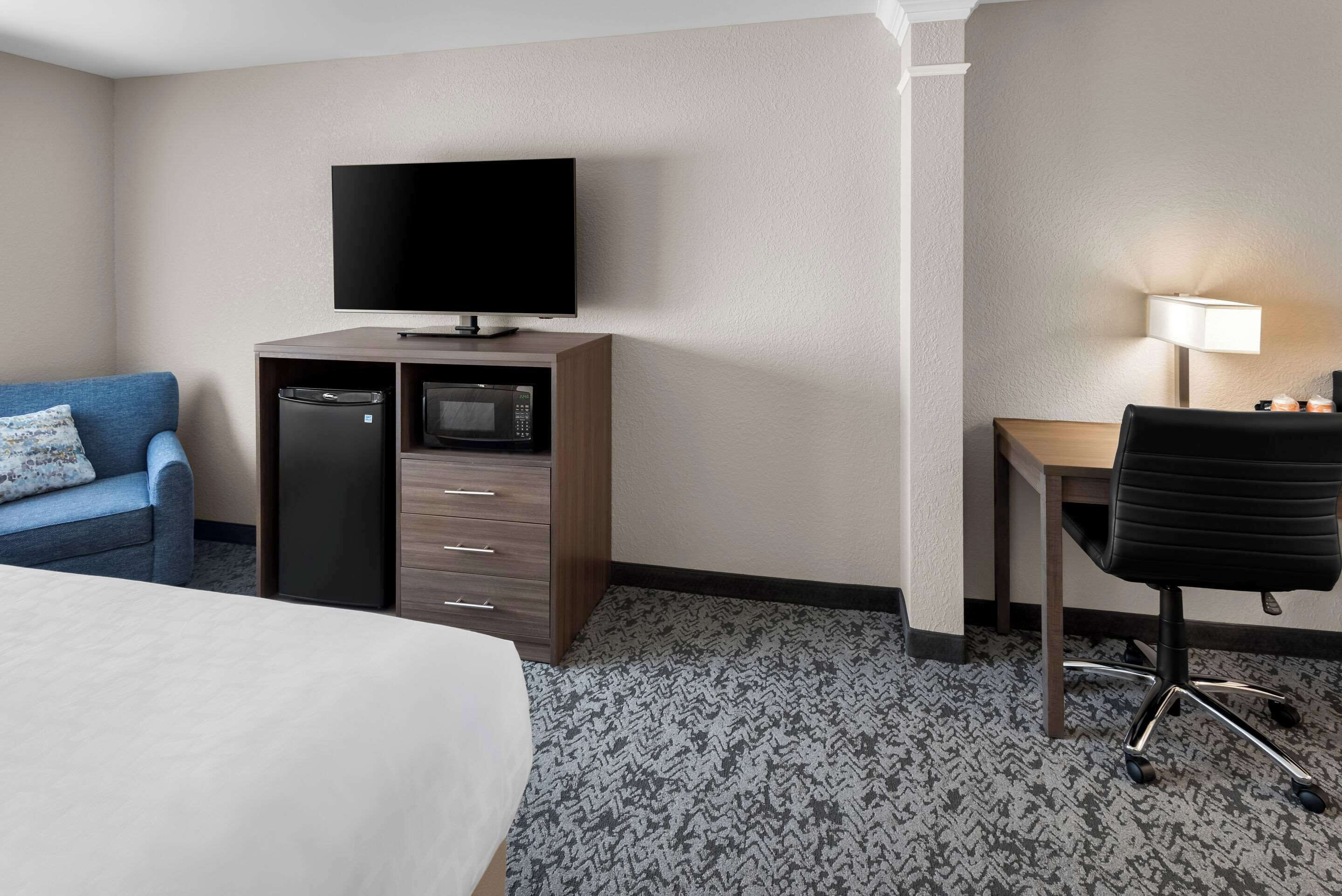 Ein Hotelzimmer mit einem Bett, einem blauen Sofa, einem Schreibtisch mit Lampe, einem Fernseher, einer Mikrowelle und einem Kühlschrank.