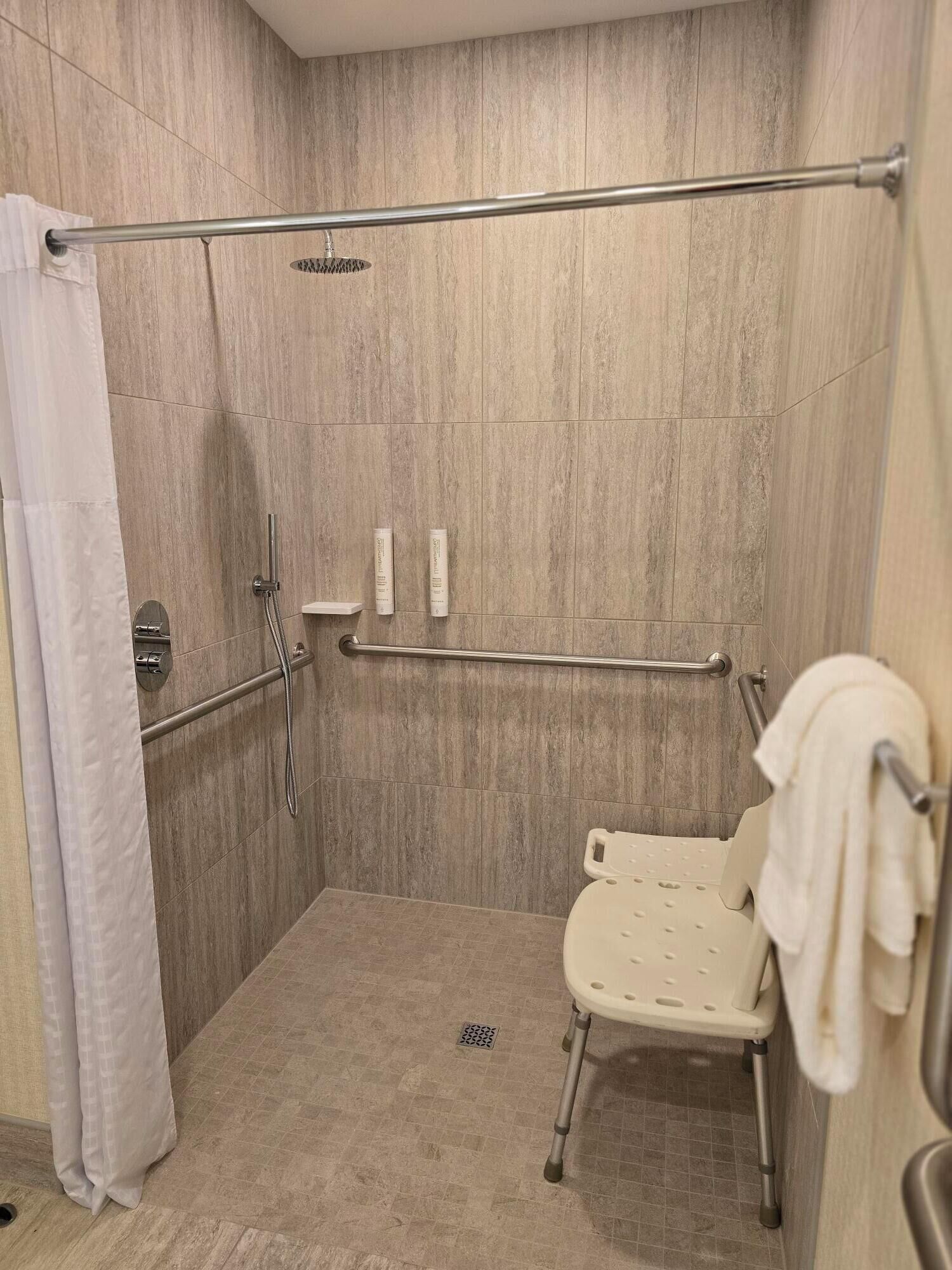A wheelchair-accessible shower stall with a grab bar, a white toilet, and a towel rack.