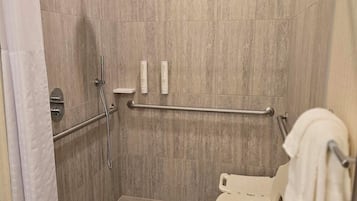 A wheelchair-accessible shower stall with a grab bar, a white toilet, and a towel rack.