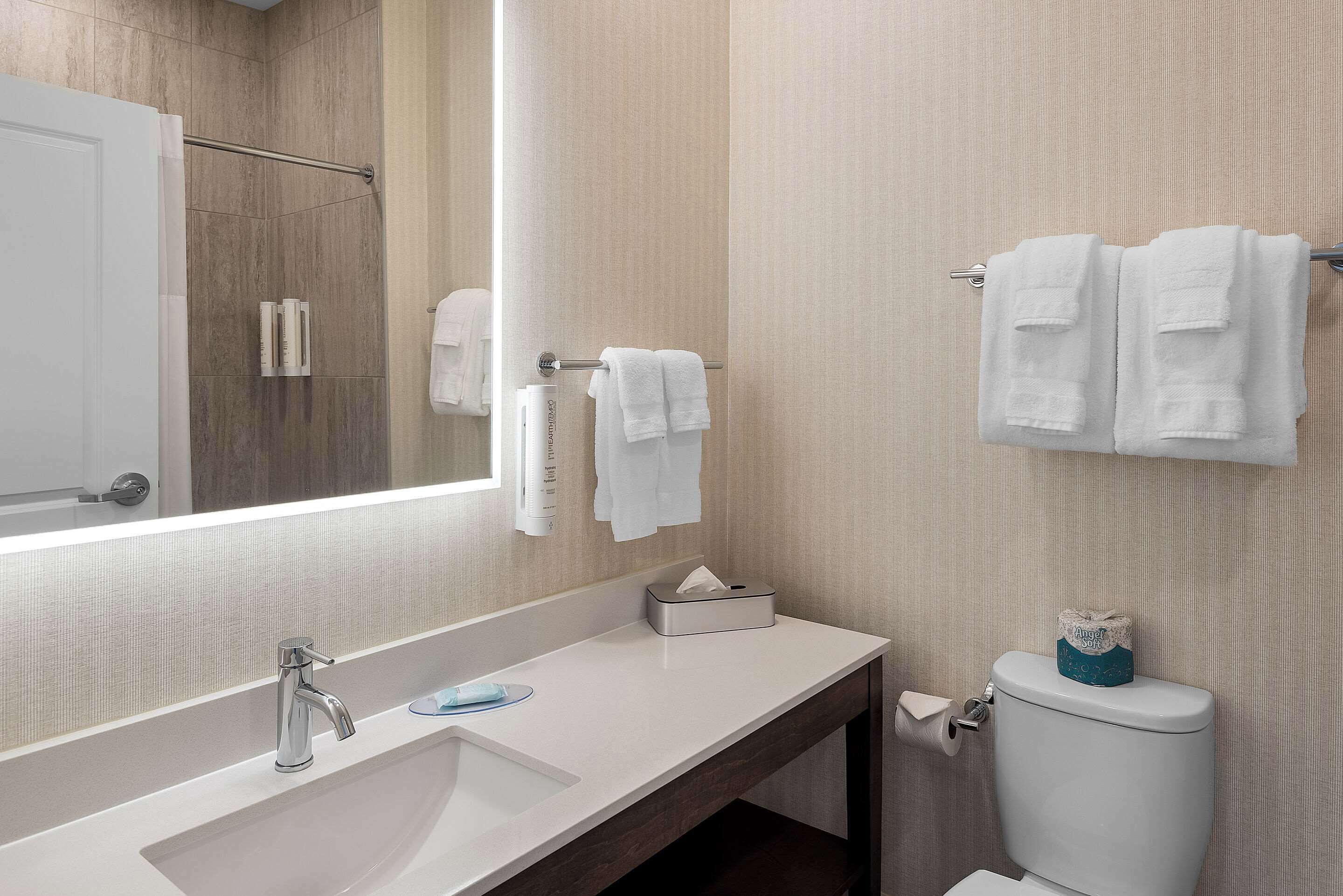 Un baño moderno con un espejo grande, un lavamanos, un inodoro y un perchero para toallas.