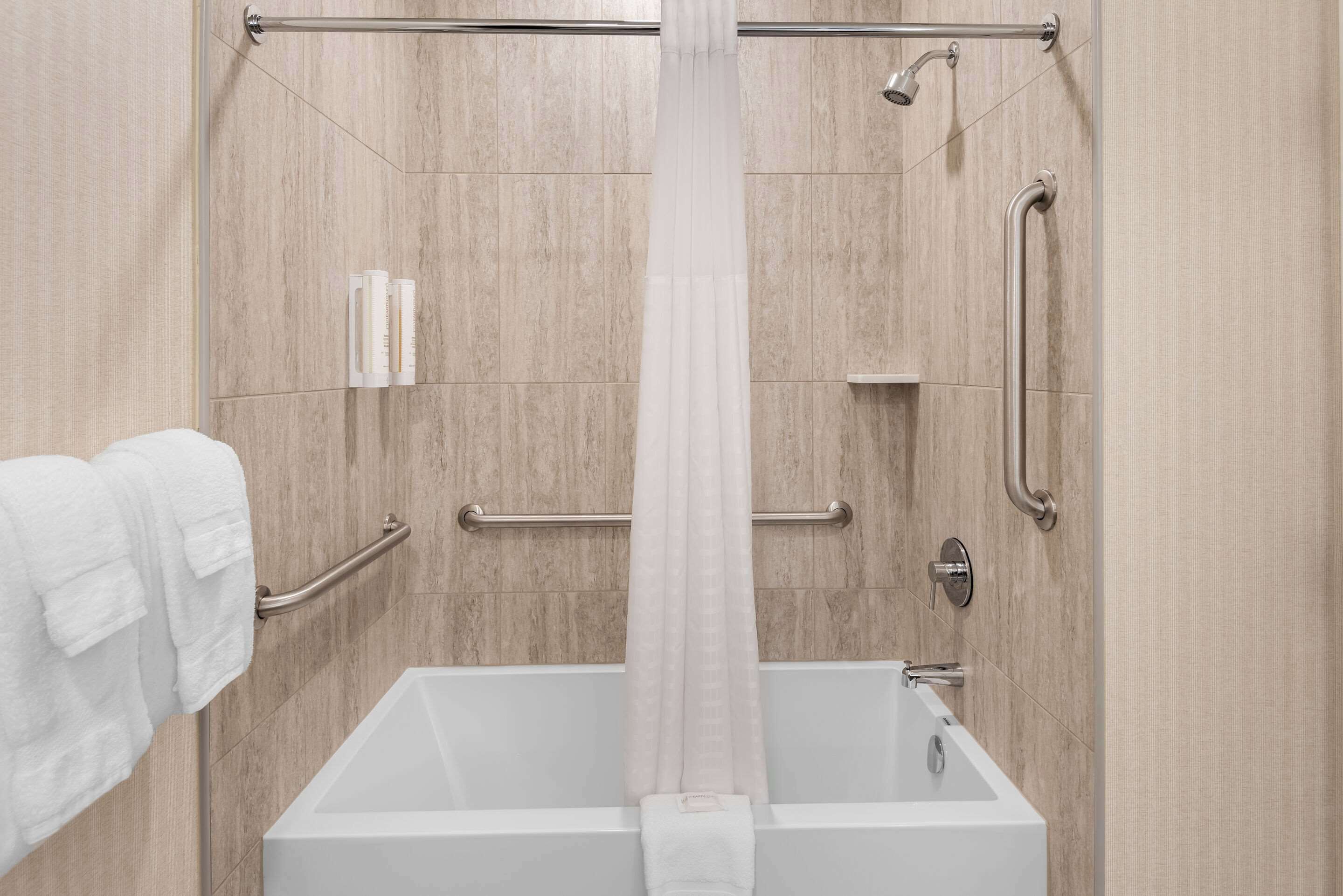 A modern bathroom with a bathtub, grab bars, and a shower curtain.
