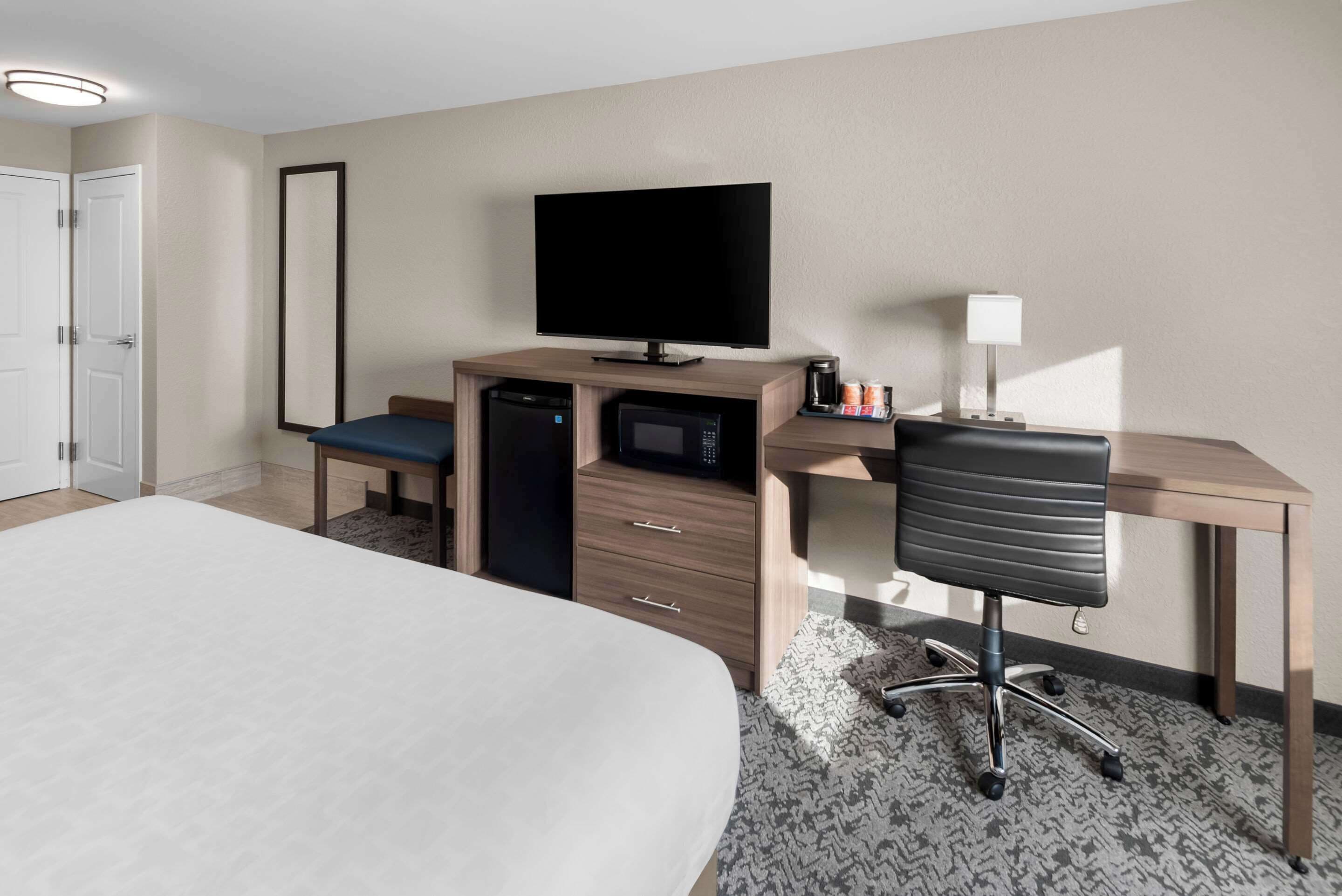 Una habitación de hotel con una cama, un escritorio con una computadora, televisor, microondas y cafetera.