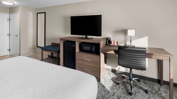 Una habitación de hotel con una cama, un escritorio con una computadora, televisor, microondas y cafetera.