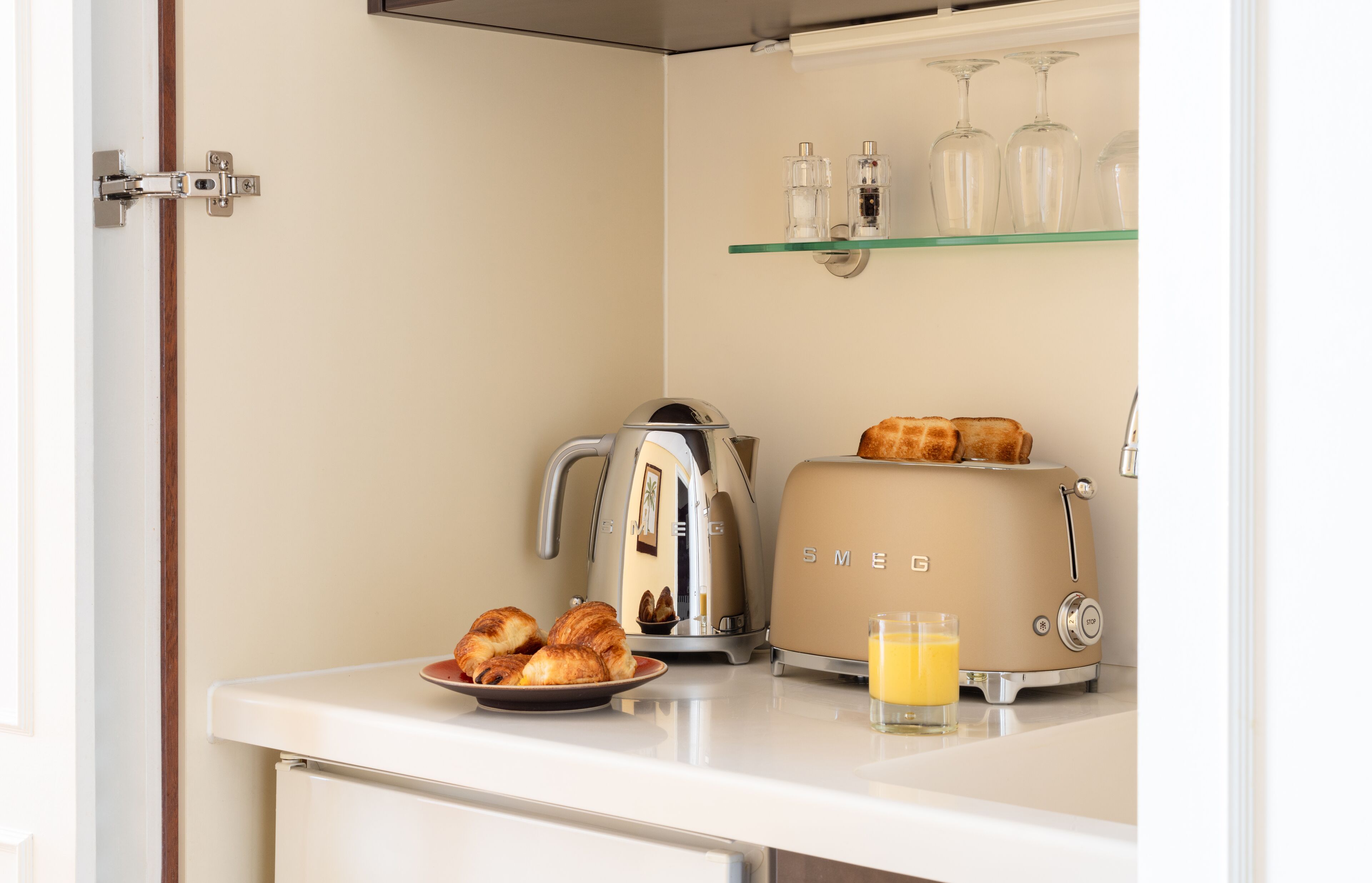 Une petite cuisine équipée d’un grille-pain, d’une bouilloire, de croissants et d’un verre de jus d’orange.