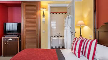 Quarto de hotel com cama, televisão, banheiro com pia e espelho, e armário.