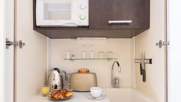 Una kitchenette compacta con microondas, tostadora, cafetera y una repisa de vidrio con tazas.